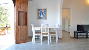 Un comedor con puerta de madera, una mesa blanca con sillas, un cuadro en la pared y un mueble para televisor.