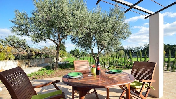 Un patio al aire libre con una mesa y sillas de madera, una botella de vino y un plato verde.