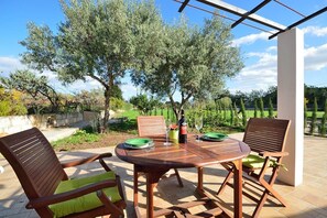Un patio al aire libre con una mesa y sillas de madera, una botella de vino y un plato verde.