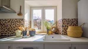 Cozinha com bancada branca, pia e janela com vista para árvores e edifícios.