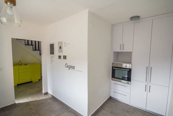 A modern kitchen with white cabinets, a built-in oven, and a bright yellow cabinet in the adjacent room.