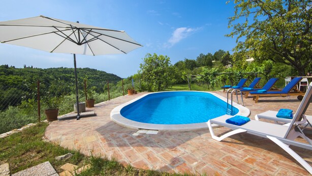 Piscina com espreguiçadeiras e um guarda-sol, cercada por vegetação e colinas.