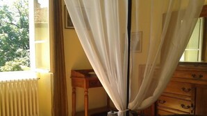 Een hotelkamer met een bed, een houten dressoir, een radiator en een raam met gordijnen.