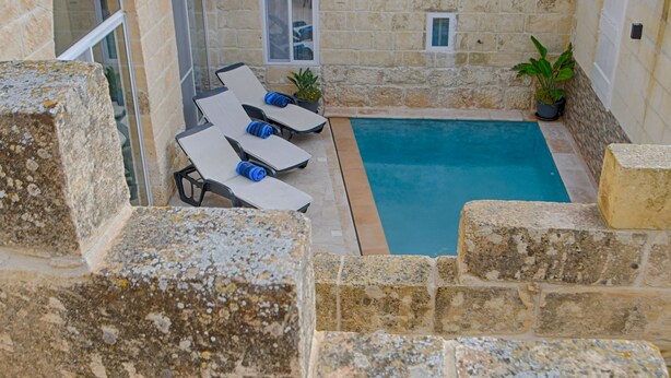 A stone courtyard with a pool, lounge chairs, and a small table. - Simar Farmhouse (Qala)