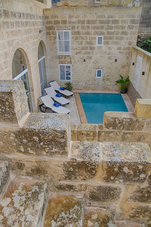 A stone courtyard with a pool, lounge chairs, and a small table. - Simar Farmhouse (Qala)