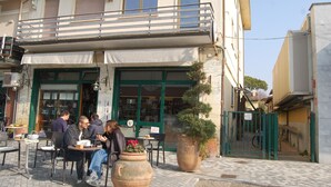 A cafe with outdoor seating, a green awning, and a potted plant in front. - VERSILIA APARTMENT (Pietrasanta)