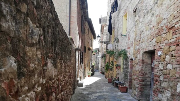 A narrow cobblestone alley with stone buildings on either side, potted plants, and a clear sky. - The Photographer's House (Colle di Val d'Elsa)