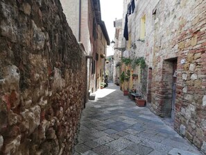 A narrow cobblestone alley with stone buildings on either side, potted plants, and a clear sky. - The Photographer's House (Colle di Val d'Elsa)