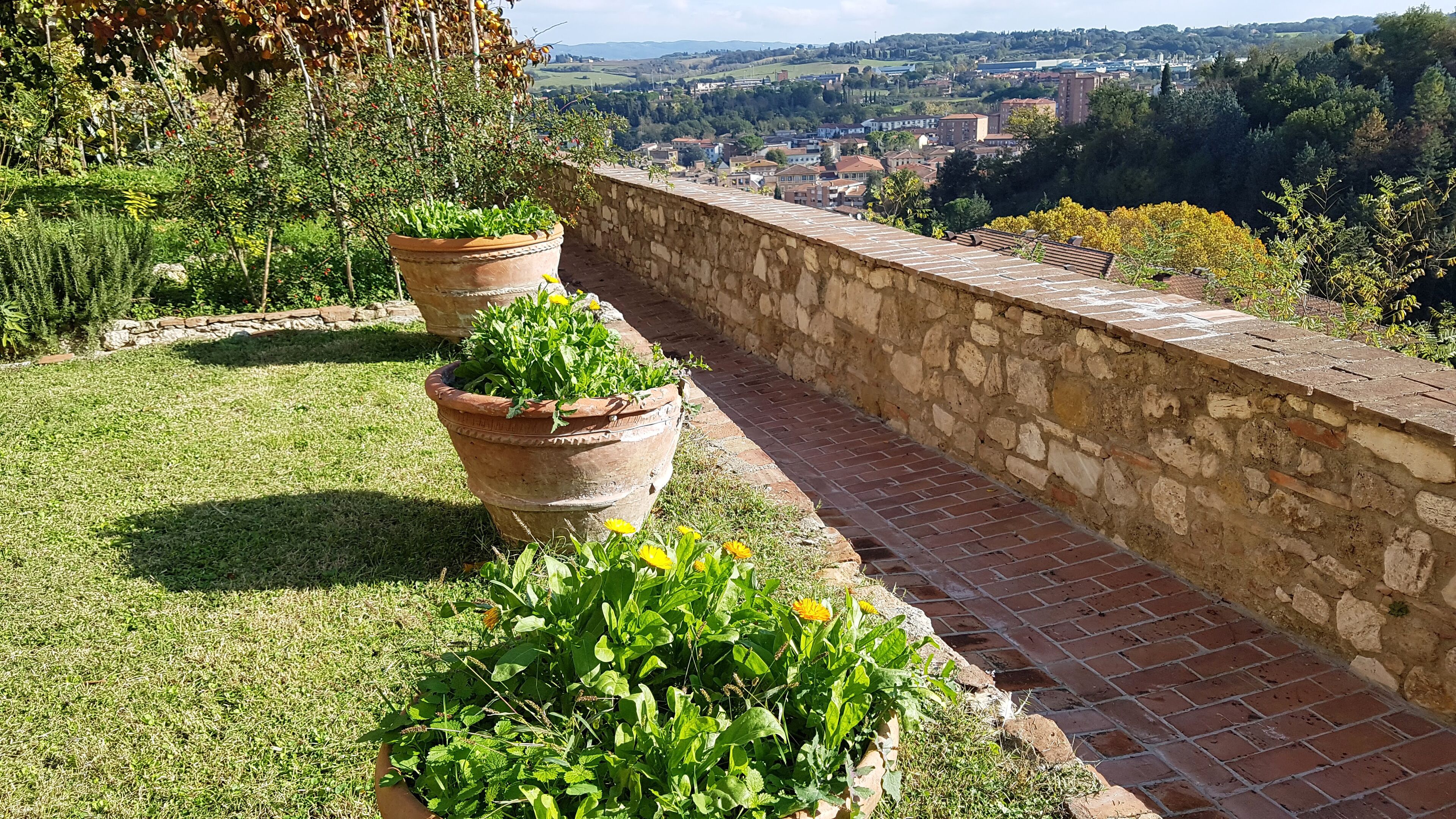 A stone wall with terracotta planters on a grassy area overlooking a town.