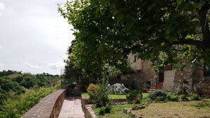 A paved pathway leading to a rustic stone building surrounded by greenery and a hill in the background. - The Photographer's House (Colle di Val d'Elsa)