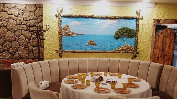A round table with a white tablecloth, surrounded by beige cushioned chairs, set against a wall with a painted seascape mural. - Carsi Otel (Trabzon)