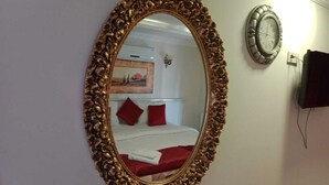 An ornate gold-framed mirror reflecting a bed with red pillows and a white blanket. - Carsi Otel (Trabzon)