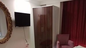 A hotel room with a wooden wardrobe, a television mounted on the wall, a red armchair, and two red beds. - Carsi Otel (Trabzon)