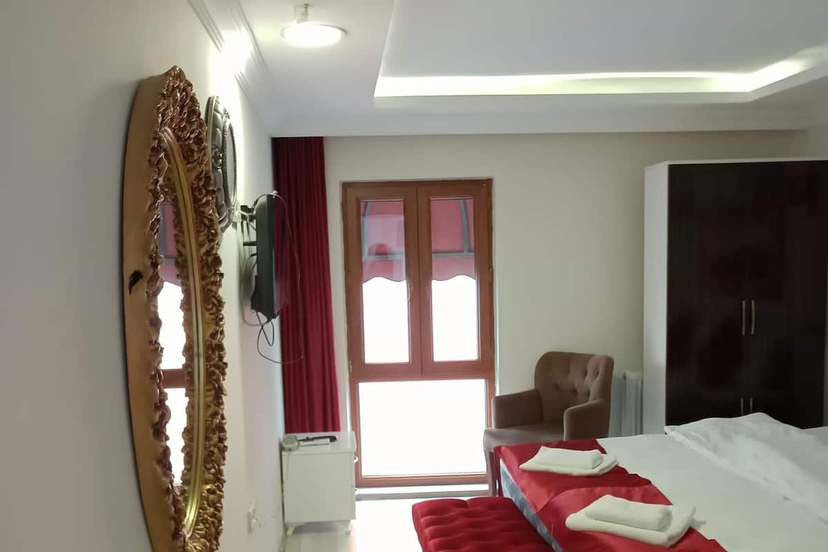 A modern bedroom with a large bed, a red bench, a wardrobe, and a large mirror.