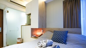 A hotel room with a bed, a nightstand, a lamp, a checkered pillow, and a basket of rolled towels. - Kactus Hotel (Kowloon)