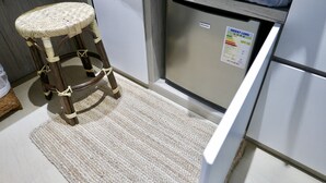 A kitchen with a wicker stool, a refrigerator with an energy label, and a white cabinet. - Kactus Hotel (Kowloon)