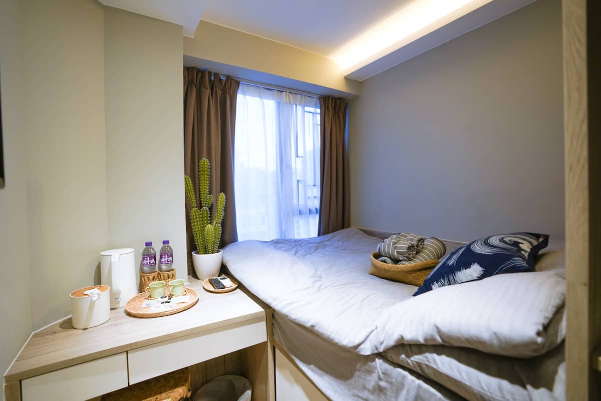 Habitación de hotel con cama, escritorio con cafetera, un cactus y ventana con cortinas.