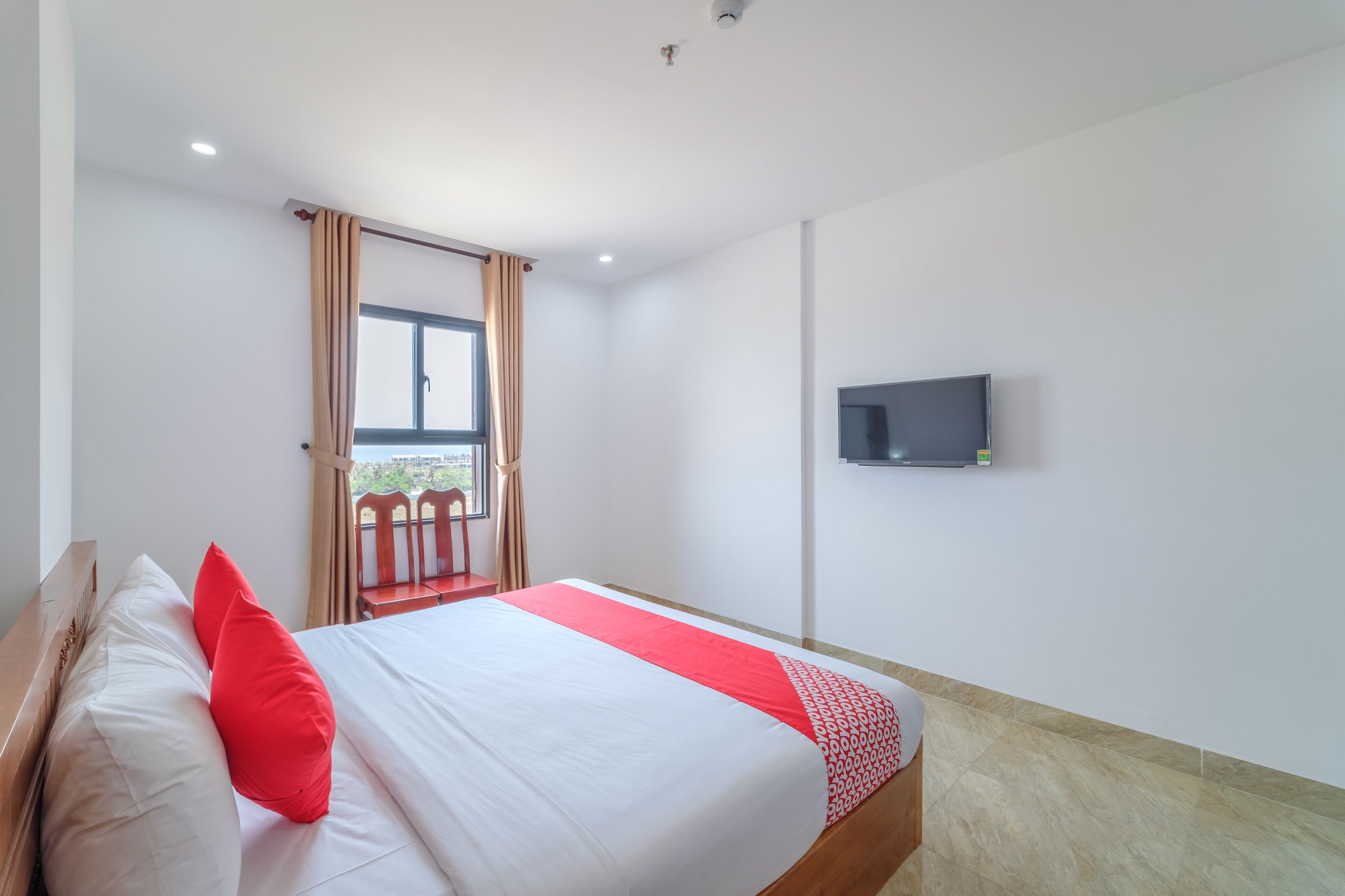 A hotel room with a bed, a TV mounted on the wall, and a window with curtains.