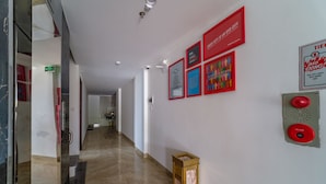 Een gang met een rookmelder en een bord met nooduitgang, een glazen deur en een muur met ingelijste posters.