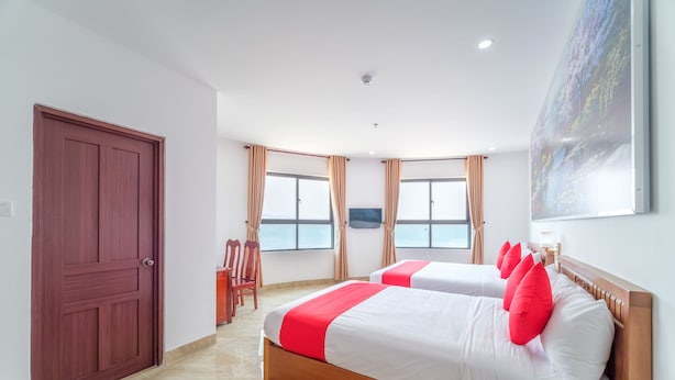 Een hotelkamer met twee bedden, een houten deur en een groot raam met gordijnen.