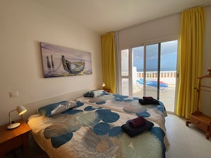 Una camera da letto con un letto, un comodino, una lampada, un quadro e vista mare tramite una porta scorrevole in vetro.