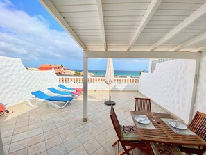 Una veranda riparata con poltrone da relax, un tavolo da pranzo per due persone e vista sull'oceano.