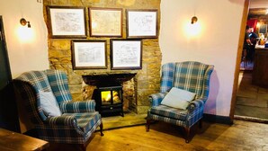 A cozy room with two plaid armchairs, a stone wall, and a fireplace. - The Hollybush Inn (Southam)