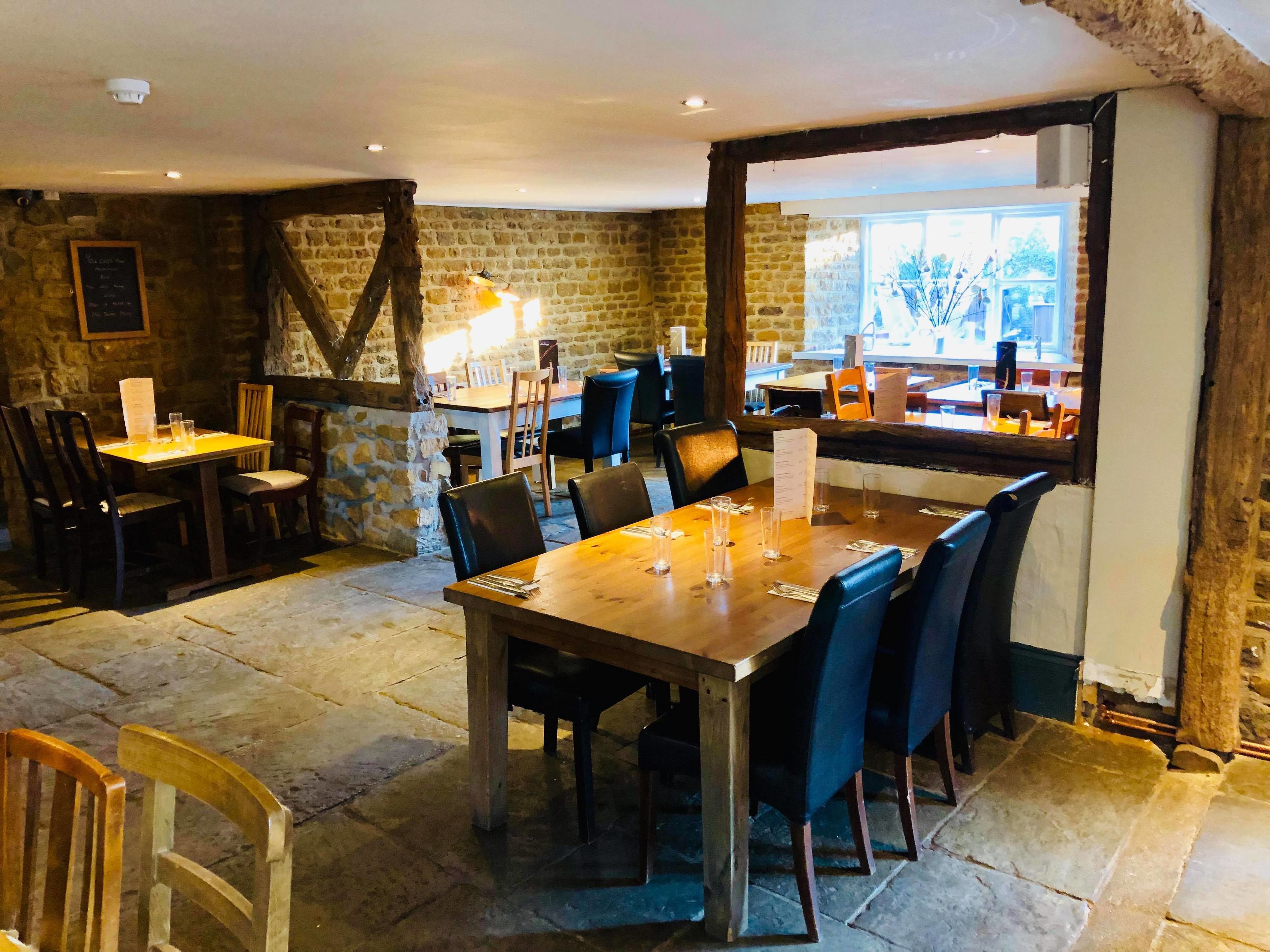 Ein Restaurant mit Steinwänden, Holztischen und schwarzen Stühlen.