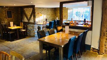 Ein Restaurant mit Steinwänden, Holztischen und schwarzen Stühlen.