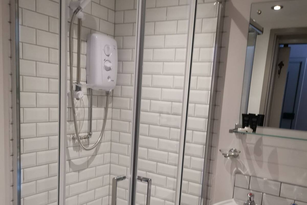 A modern bathroom with a glass-enclosed shower, white tiled walls, and a white sink with a mirror above it.