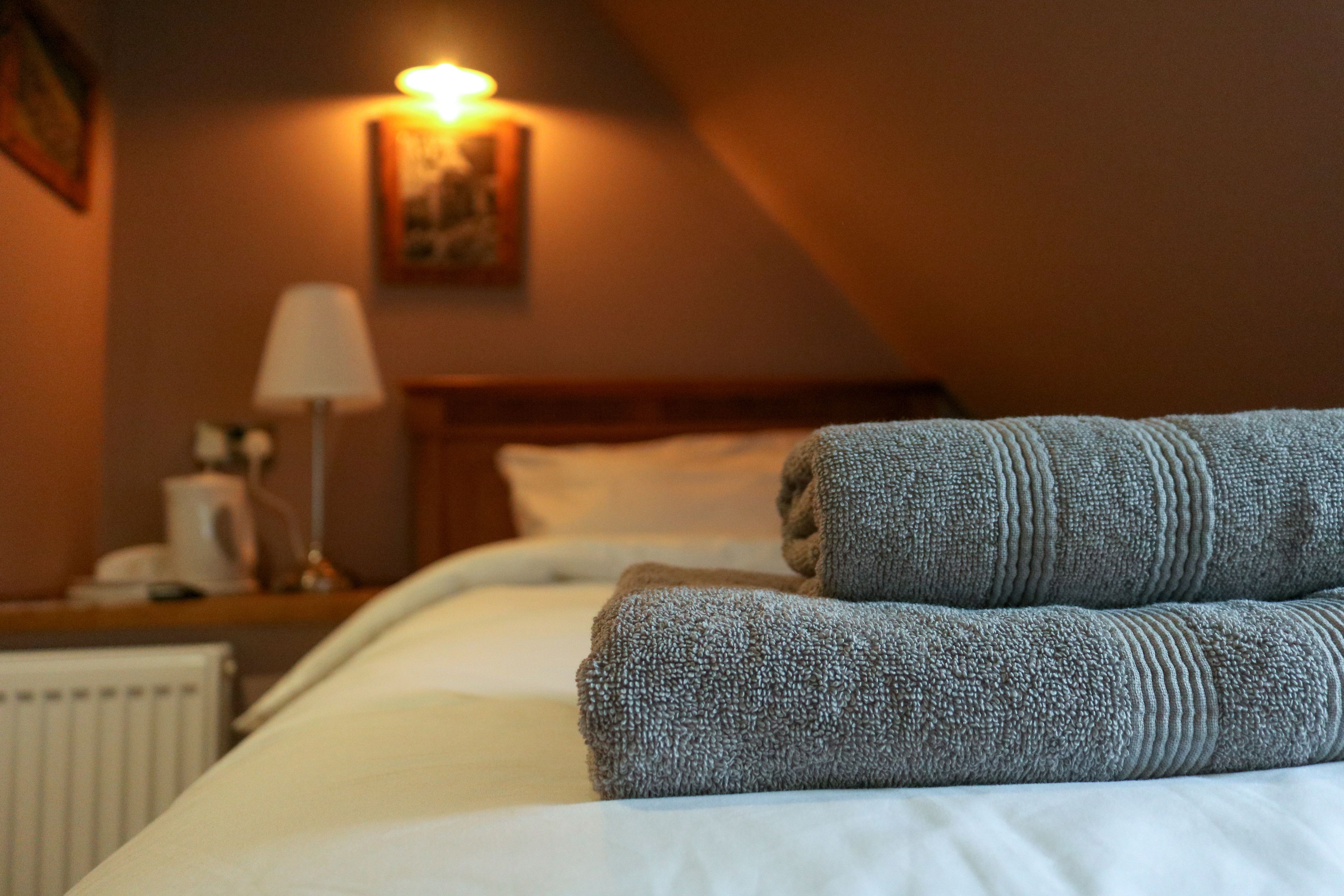 Een keurig opgemaakt bed met gevouwen handdoeken, een bedlamp en een ingelijst foto aan de muur.