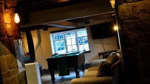A cozy room with a pool table, a comfortable armchair, and a large window with a view. - The Hollybush Inn (Southam)