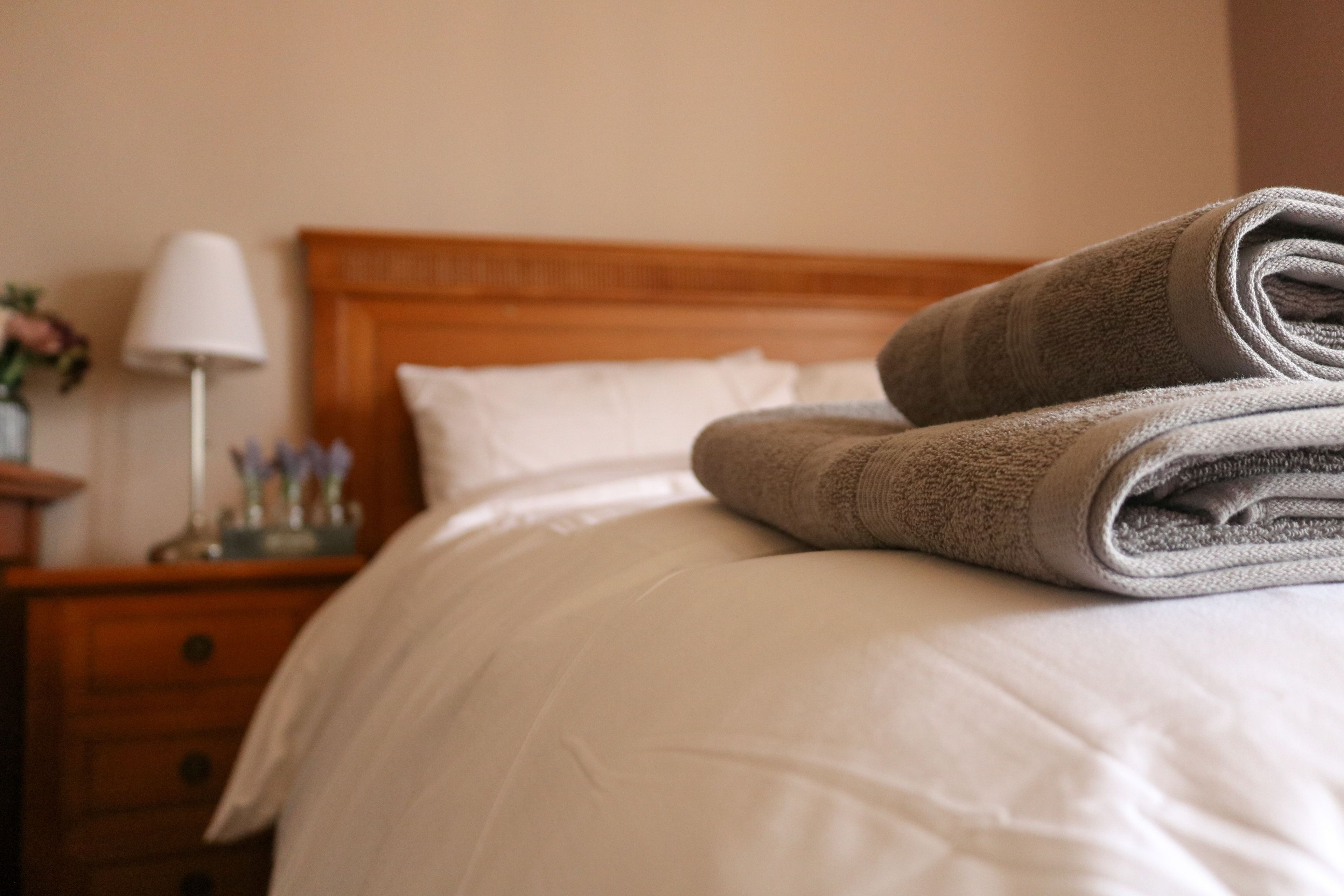 Een netjes opgemaakt bed met een gevouwen handdoek en een wit kussen.