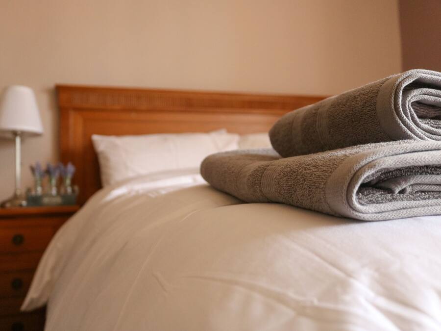 Een netjes opgemaakt bed met een gevouwen handdoek en een wit kussen.