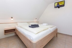 A bedroom with a wooden bed, a nightstand, a wall-mounted TV, and a small shelf.