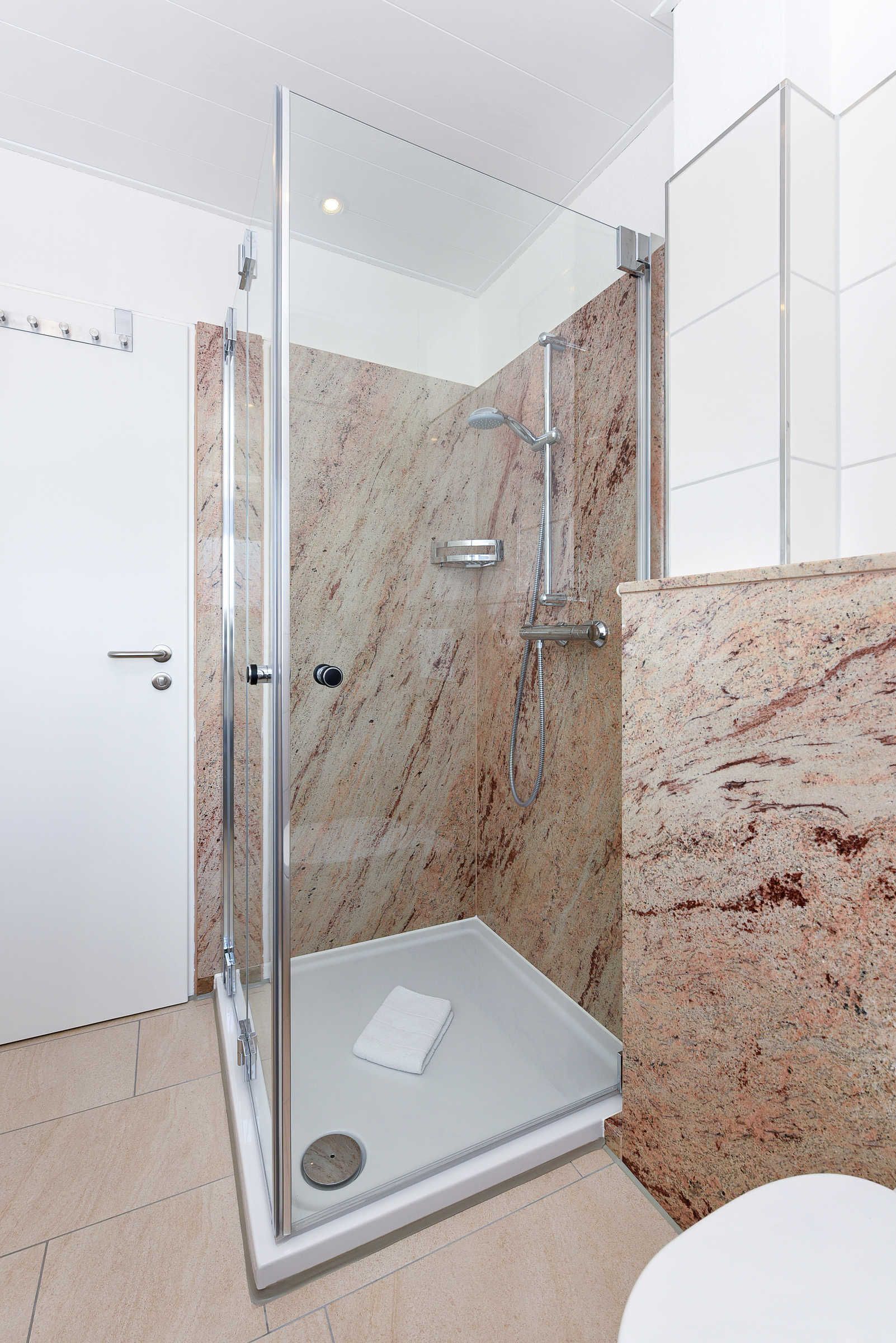 Um banheiro moderno com chuveiro em cabine de vidro, paredes de mármore e vaso sanitário branco.
