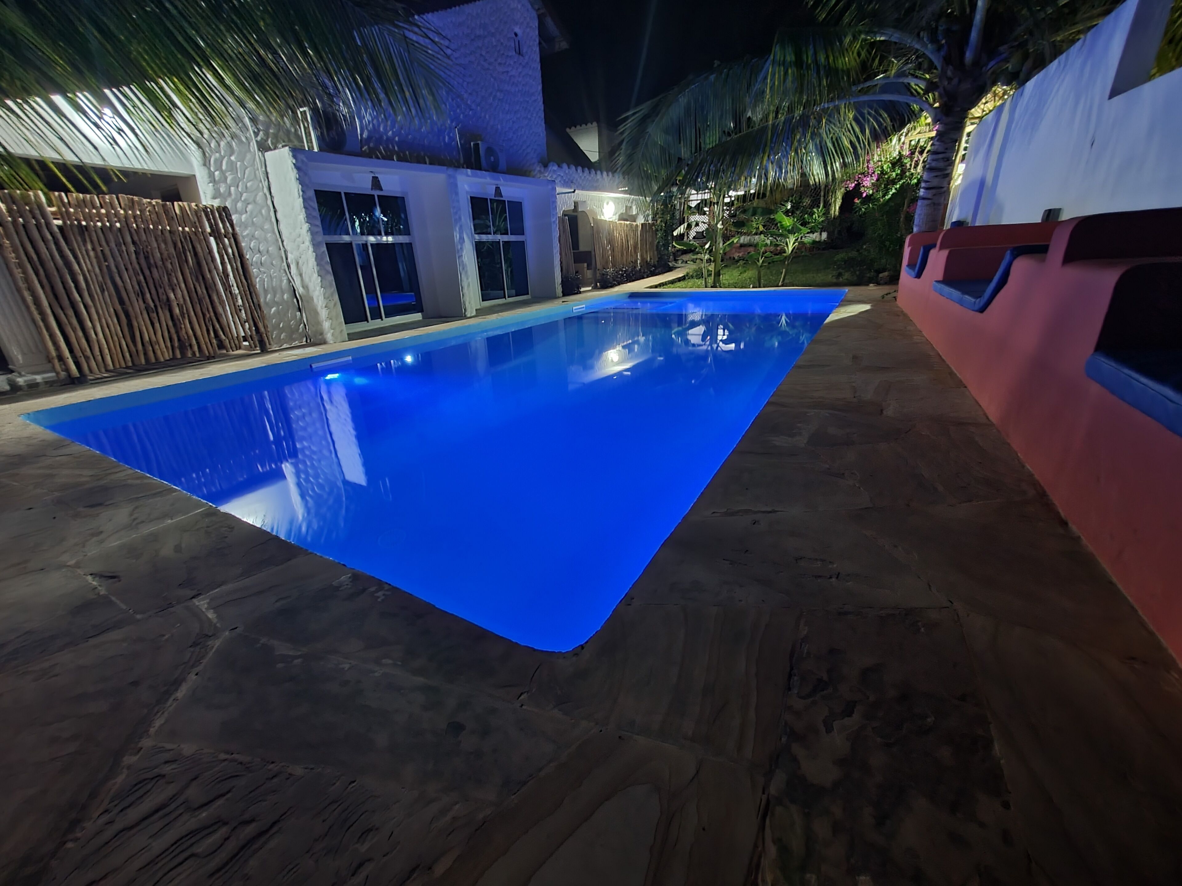 Una piscina con revestimiento azul, rodeada por una terraza de piedra y palmeras.
