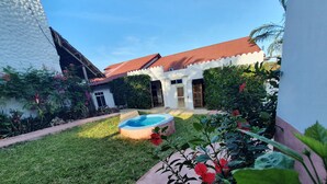 A backyard with a swimming pool, a grassy lawn, and a white building with a red roof. - Baridi Villa (Kiwengwa)
