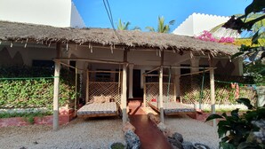 A traditional thatched-roof structure with two elevated beds, a gravel pathway, and surrounding greenery. - Baridi Villa (Kiwengwa)