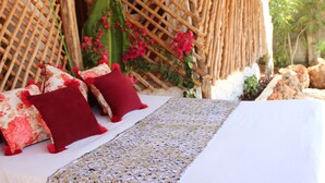 A bed with a patterned bedspread and two red pillows, a woven bamboo headboard, and pink flowers in the background. - Baridi Villa (Kiwengwa)