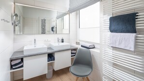 Ein modernes Badezimmer mit zwei Waschbecken, einem Spiegel, einer Dusche und einem Handtuchhalter.