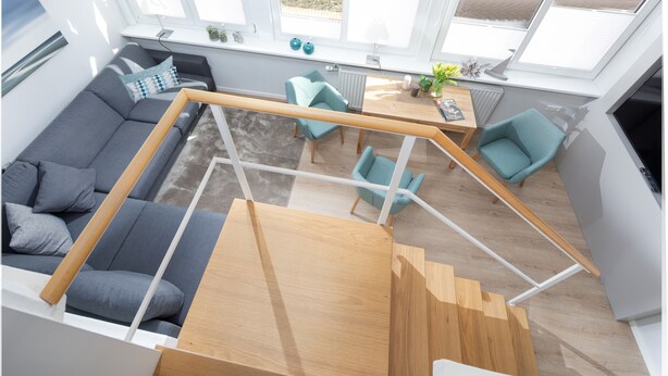 Ein modernes Interieur mit Treppe, grauem Sofa, türkisfarbenen Sesseln und einem Holztisch.