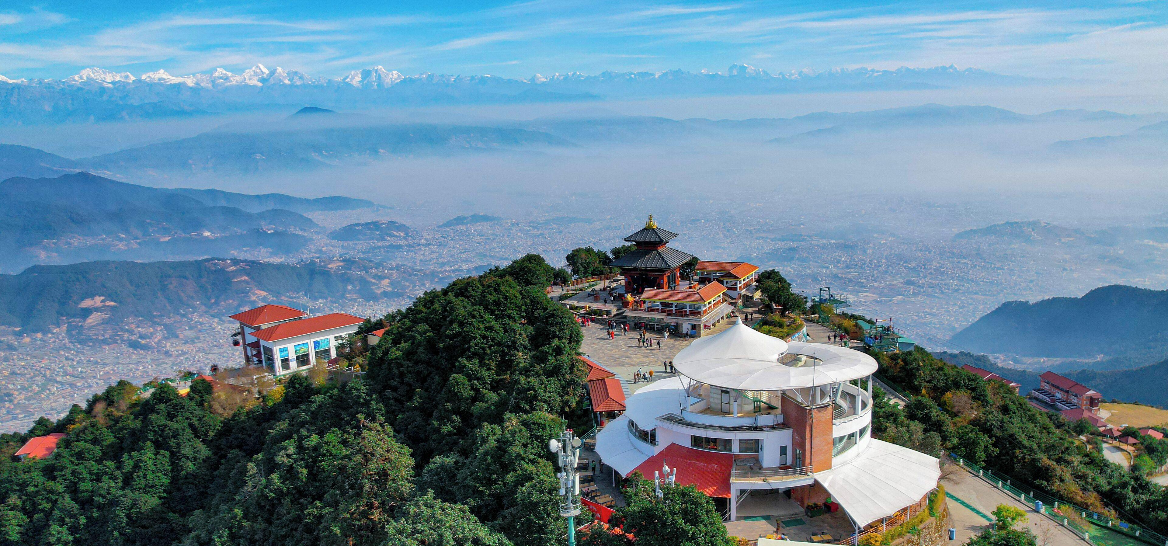 A panoramic view of a mountainous region with a traditional pagoda-style building surrounded by lush greenery.
