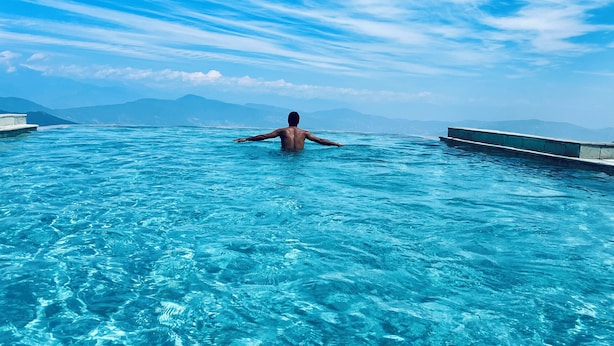 Una persona en una piscina grande y transparente de color azul, con vistas a montañas en la distancia.