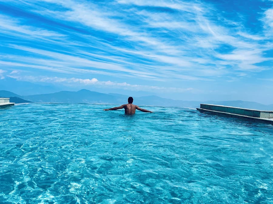 A person in a large, clear blue pool with a view of mountains in the distance.