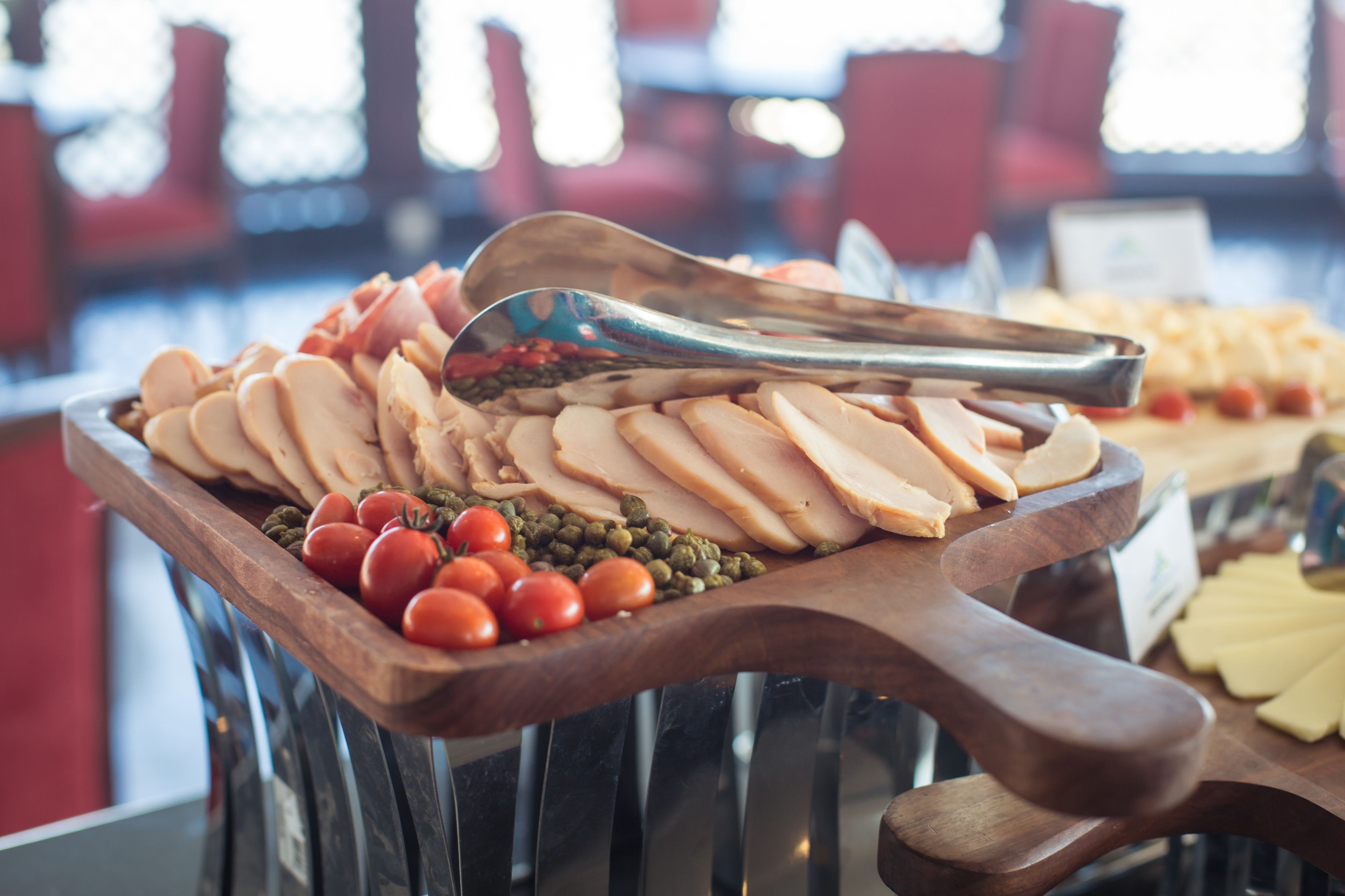 A wooden serving board with sliced meats, cherry tomatoes, and capers.