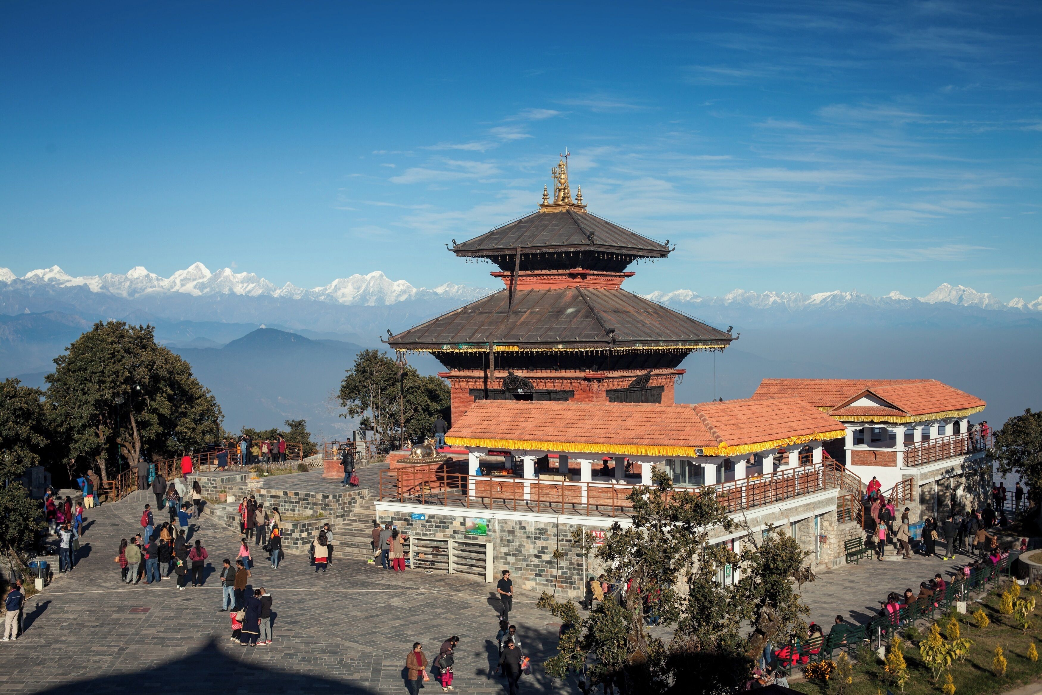 A traditional multi-tiered building with a tiled roof, surrounded by a stone-paved courtyard with visitors.