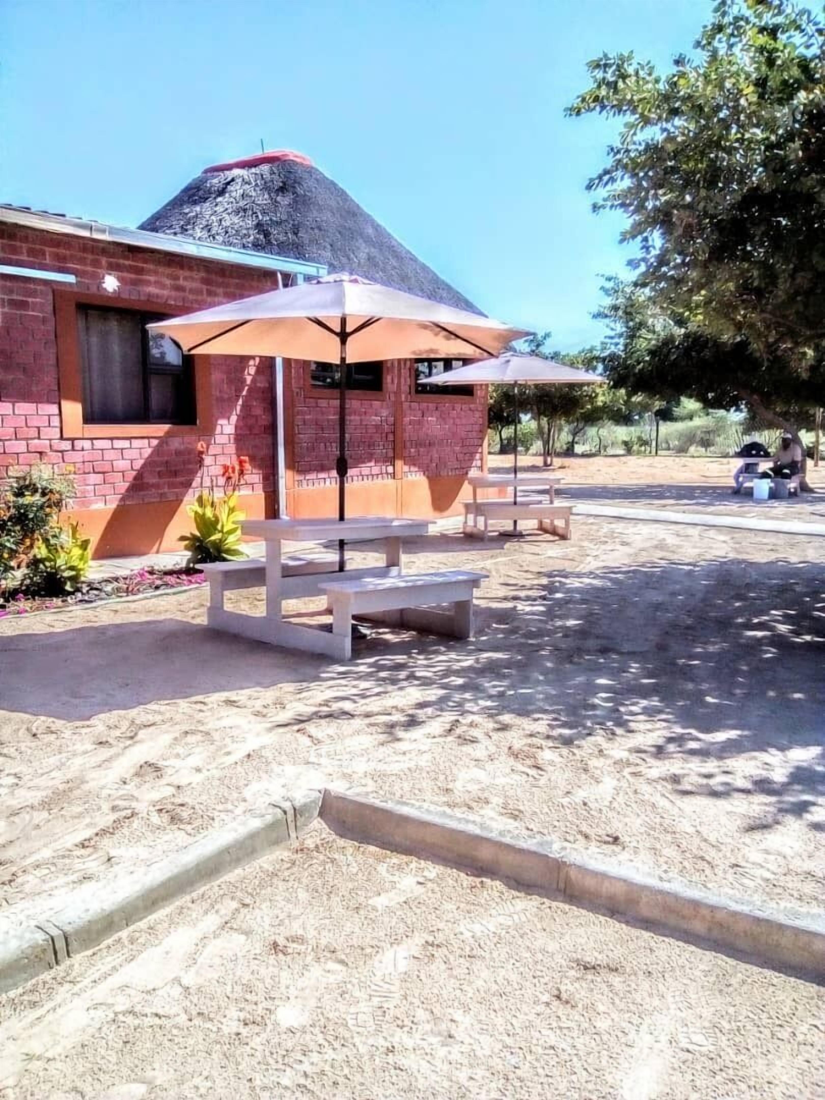 Un bâtiment à la façade en briques, doté d’une terrasse avec des parasols et dont le sol est recouvert de sable.