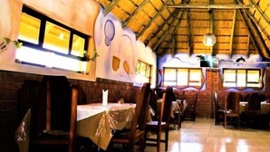 Un restaurant avec des tables et des chaises en bois, un sol carrelé et un toit de chaume.
