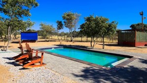 Une piscine rectangulaire bordée de bleu, entourée de galets et de chaises en bois.